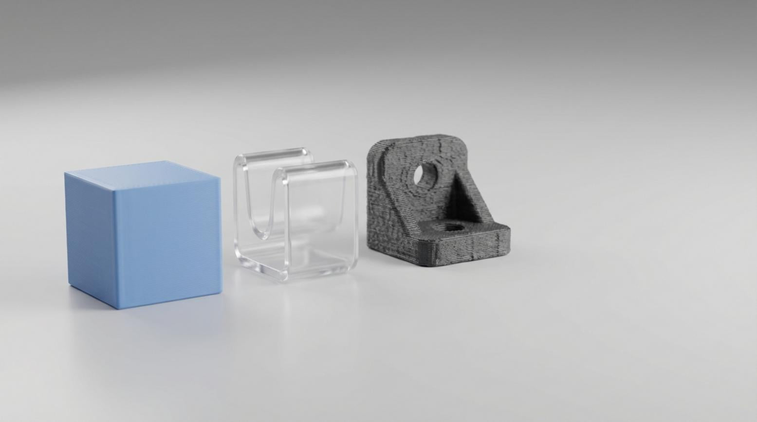 Drie 3D geprinte testonderdelen van PLA PETG en ABS naast elkaar op een lichte studioachtergrond met zichtbare laaglijnen en zachte schaduwen