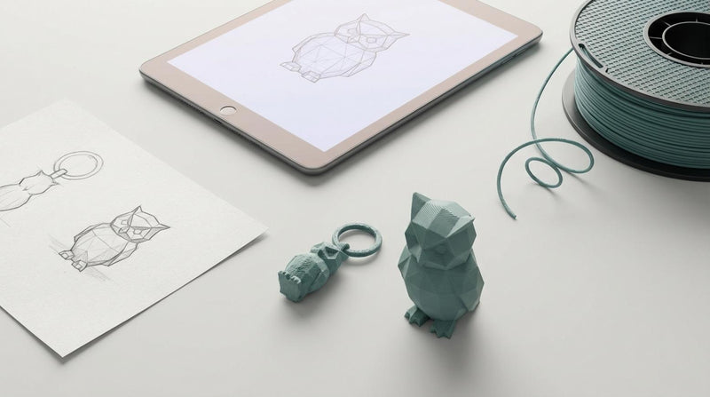 Flatlay van 3D printproces met schets, tablet met CAD, filamentspoel en afgewerkte prints op lichtgrijze achtergrond